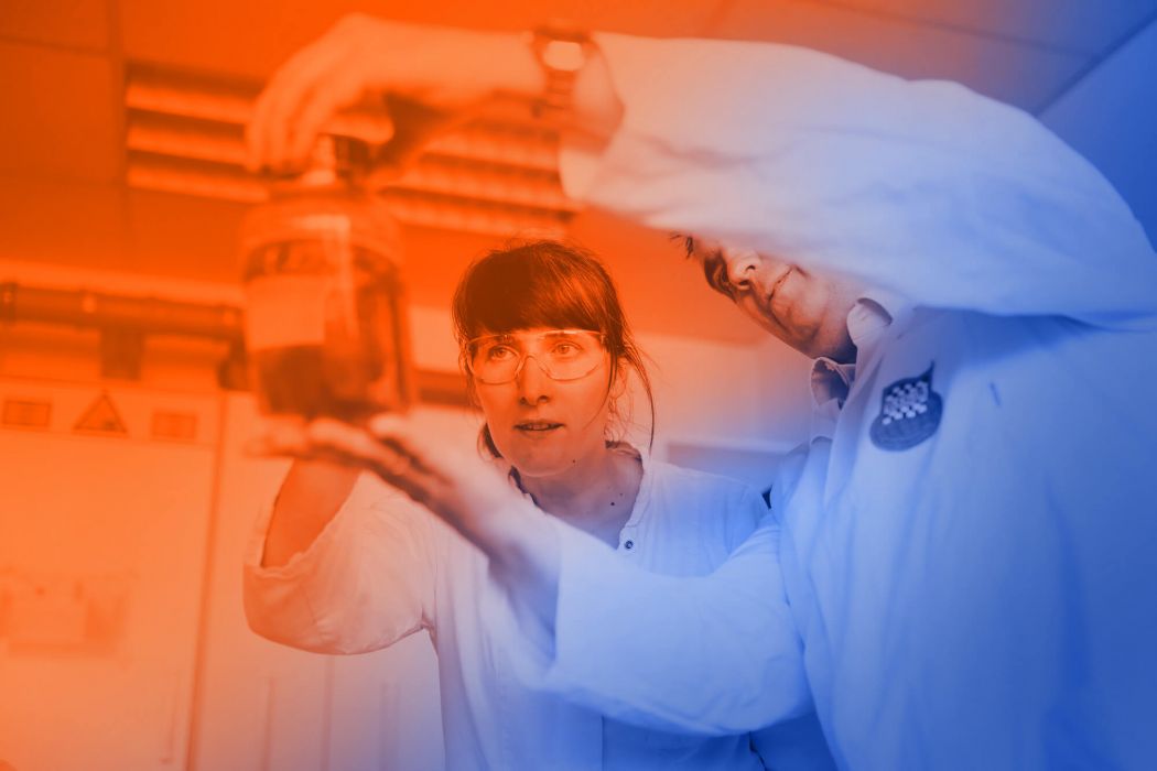 Ein Mann und eine Frau betrachten eine Schmiermittelprobe in einem Glas.