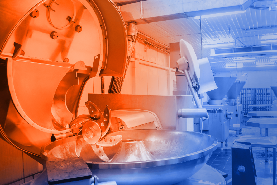 View into a meat processing factory for the production of sausages and meat products. In front is an industrial cutter for grinding meat. In the background are other machines for meat processing.