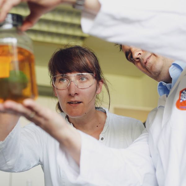 Ein Mann und eine Frau betrachten eine Schmiermittelprobe in einem Glas.