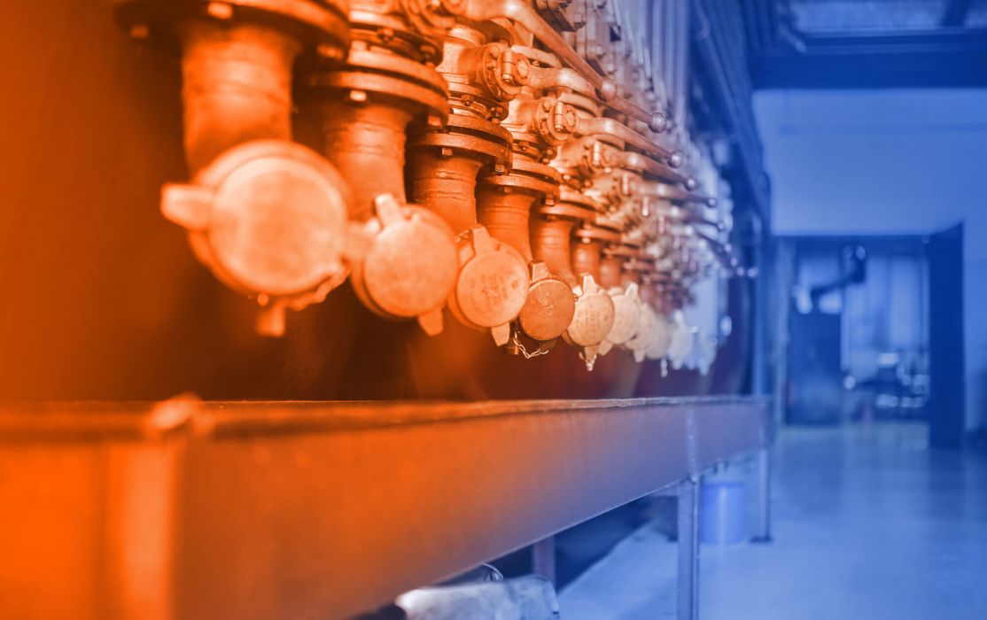 Lubricating oil and lubricant filling system at ELKALUB. A row of pipes with safety closures, valves and metering taps. In the background is a large gate leading into the adjoining hall.