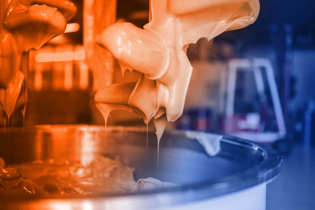 Schmierfettherstellung bei ELKALUB. Nahaufnahme in eine Produktionsmaschine mit rotierenden Mischköpfen. Diese ragen aus einem Mischzylinder und sind mit Schmierstoff bedeckt.