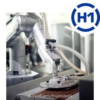 An industrial robot with hoses and a pneumatic device in food production. It reaches onto a conveyor belt and positions the chocolate bar. The H1 logo is shown at the top right.